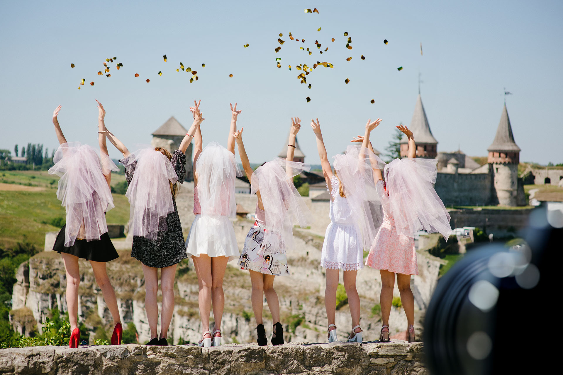 Sechs Frauen stehen mit dem Rücken zum Betrachter. Sie tragen pinke Brautschleier und werfen Konfetti in die Luft. Ein Filmdreh von JGA-Film mit einer großen JGA-Gruppe