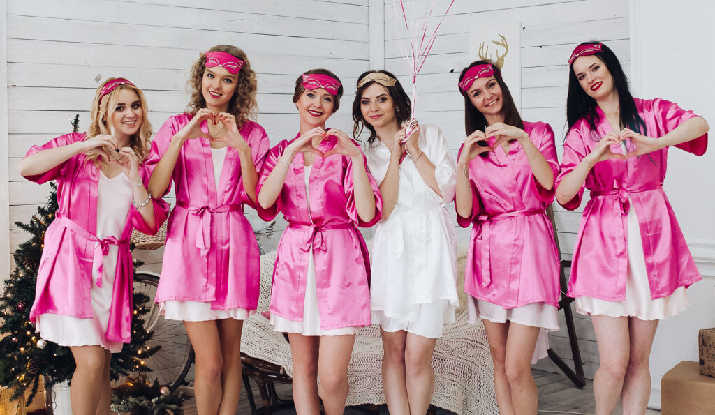 Eine Gruppe Mädels in pinken Bademänteln vor einer weißen Wand posiert für ein JGA-Foto