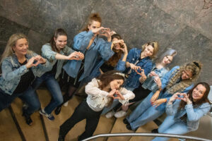 Eine Gruppe Mädels posiert auf einer Treppe für einen JGA Filmdreh. Die Mädels tragen Jeansjacken, die Braut eine weiße Bluse und ein Krönchen. Sie zeigen mit den Händen geformte Herzchen zur Kamera