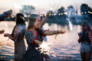 Eine Gruppe Mädels feiert einen JGA (Jungegesellinnenabschied) an einem See. Es ist Abend, Lichterketten und Wunderkerzen erhellen das Bild. - Mein JGA Film.